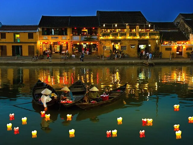 Boats with people on a river at night surrounded by floating lanterns.