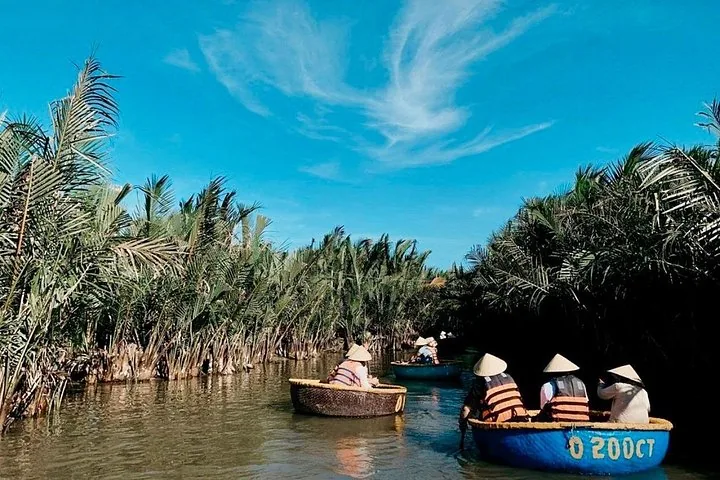 People in traditional basket boats navigating a narrow waterway lined with palms.